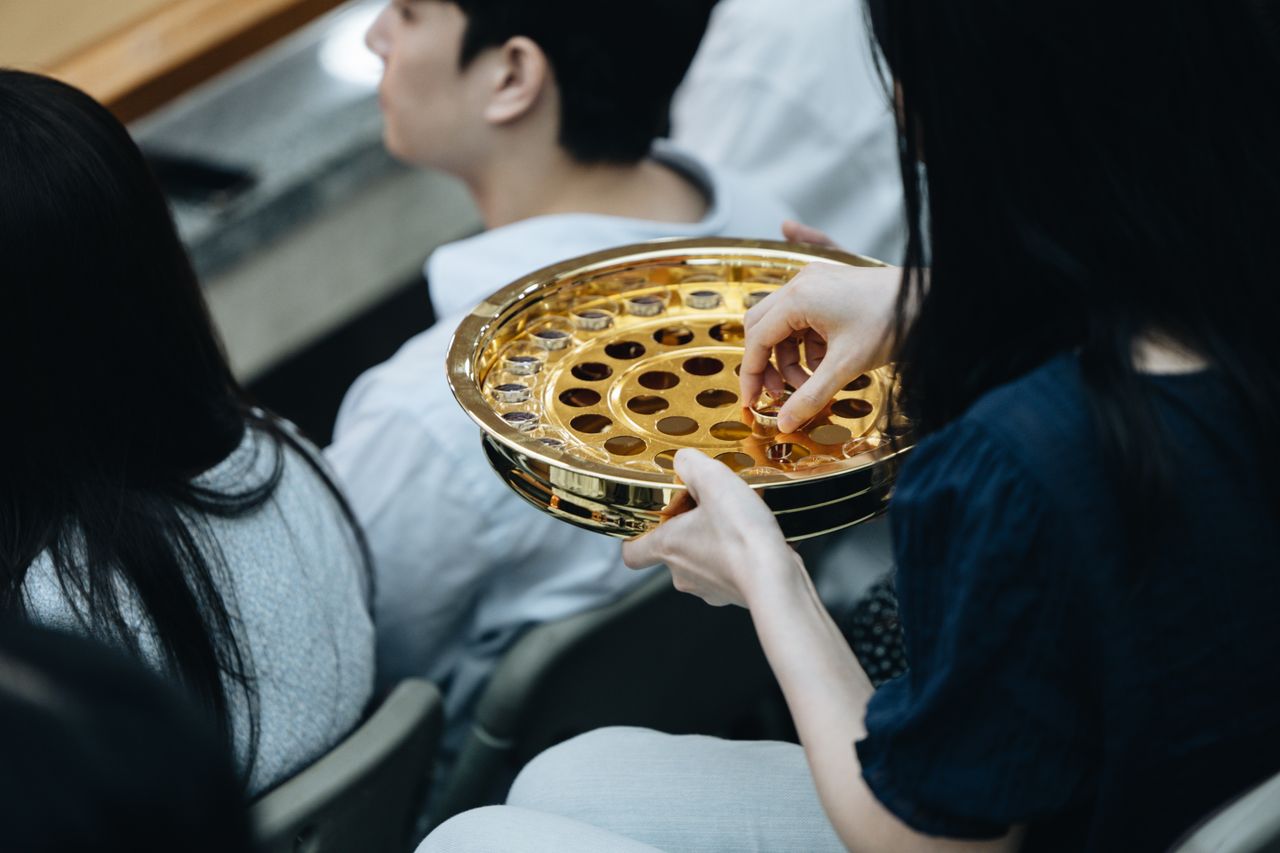 about-us-02 A golden communion plate is passed during a church service, reflecting the act of worship.